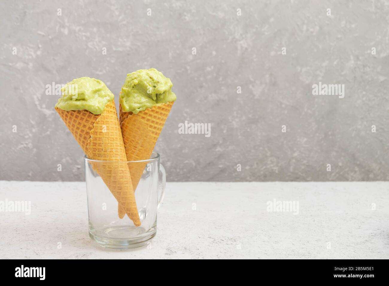 Waffelkegel mit gesunder grüner Avocado-Eiscreme auf neutralem grauem Hintergrund mit Platz für Kopien Stockfoto