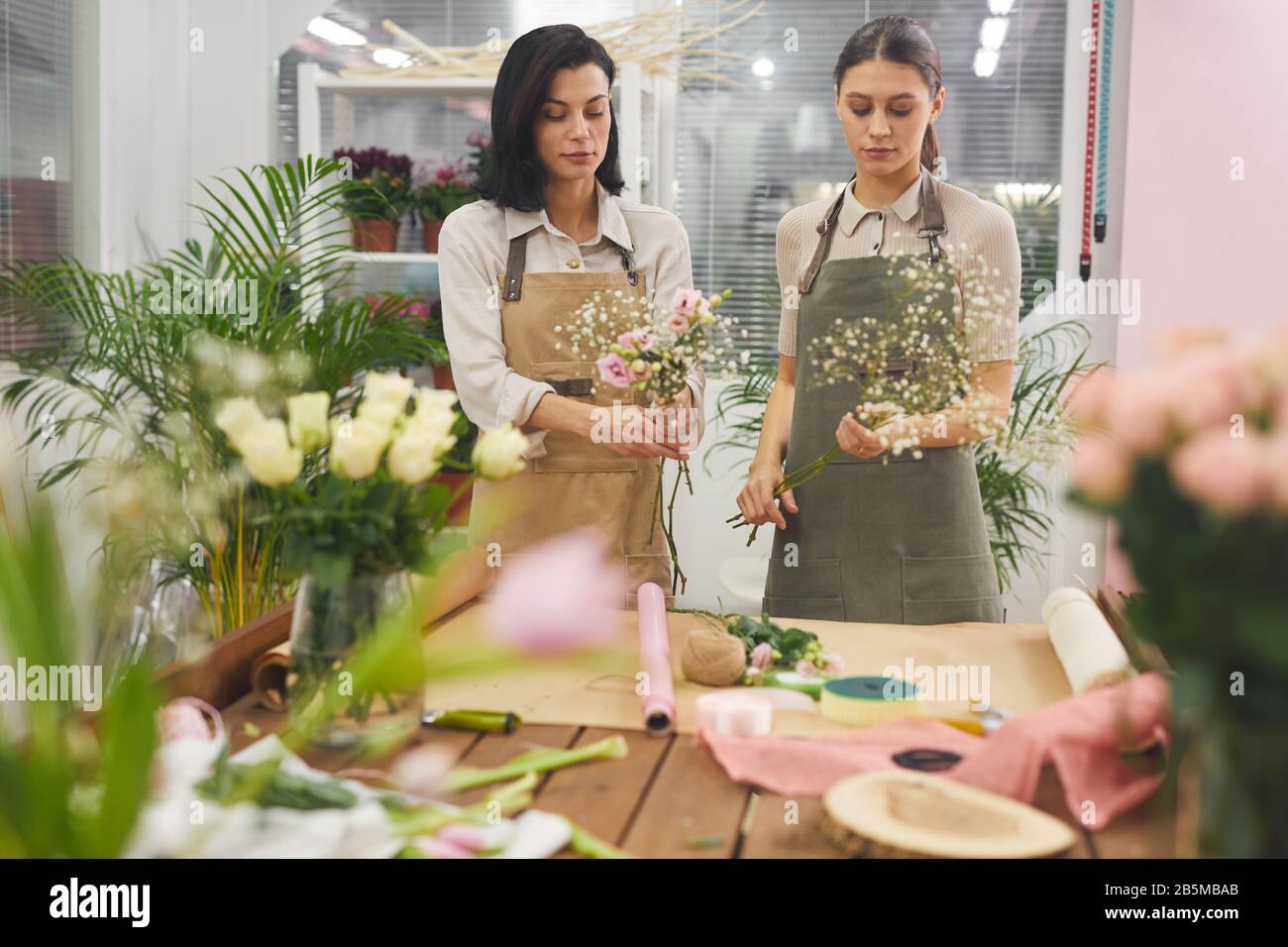 Taille hoch Porträt von zwei kreativen jungen Frauen, die Blumensträuße und Blumenkostümchen arrangieren, während sie in Blumenladen arbeiten, Kopier Raum Stockfoto