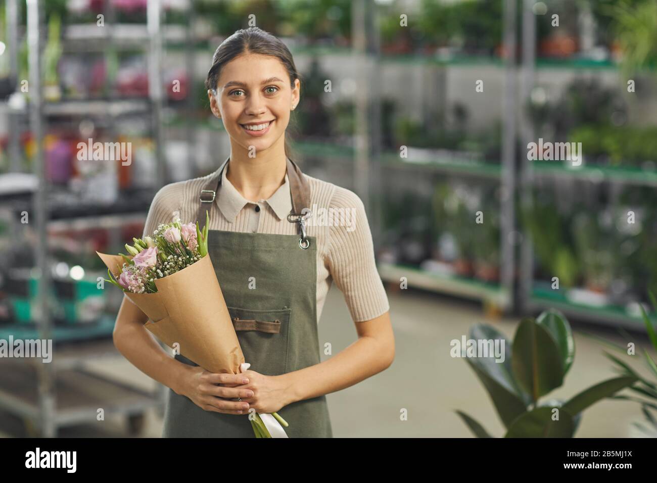 Taille hoch Porträt der lächelnden jungen Frau, die Blumenstrauß hält, während sie im Blumenladen steht, Kopierer Stockfoto