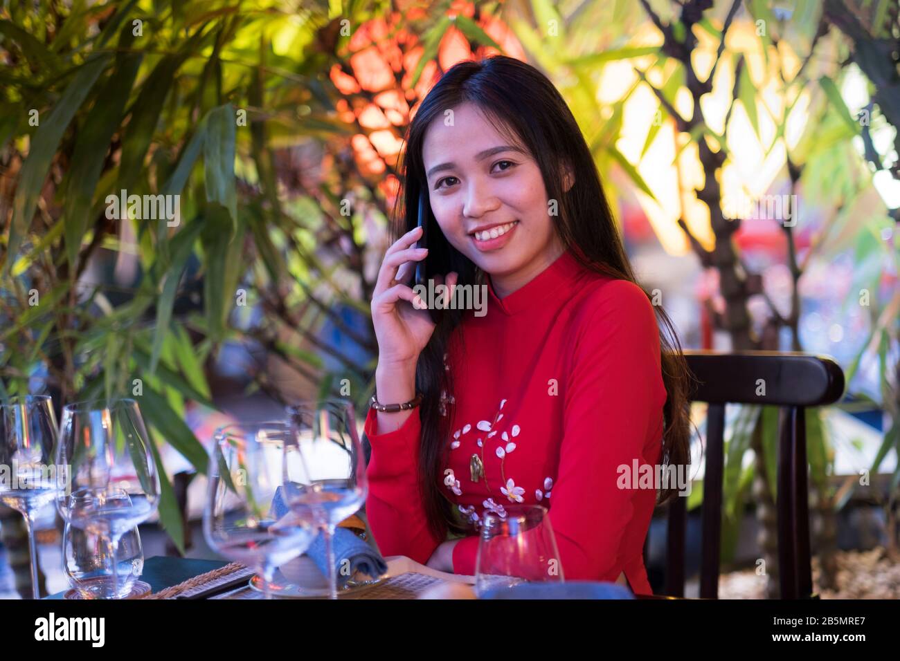 Eine junge Vietnamesin, die mit ihrem Handy ein traditionelles rotes Ao Dai Kleid trägt Stockfoto