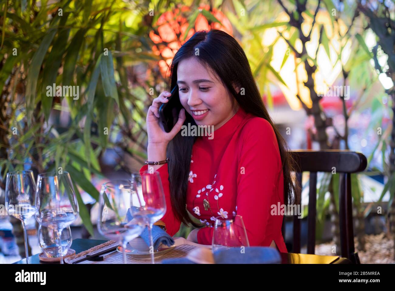 Eine junge Vietnamesin, die mit ihrem Handy ein traditionelles rotes Ao Dai Kleid trägt Stockfoto