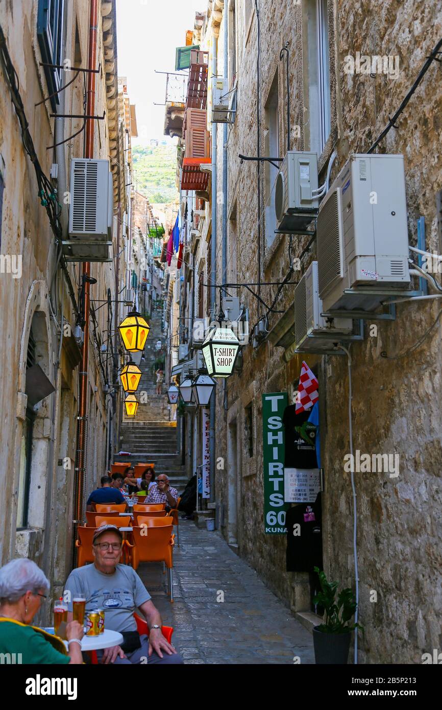 Leute, die in einer Außenbar oder einem Café in der schmalen Straße namens Ulica Naljeskoviceva sitzen, in der Altstadt von Dubrovnik, Kroatien Stockfoto