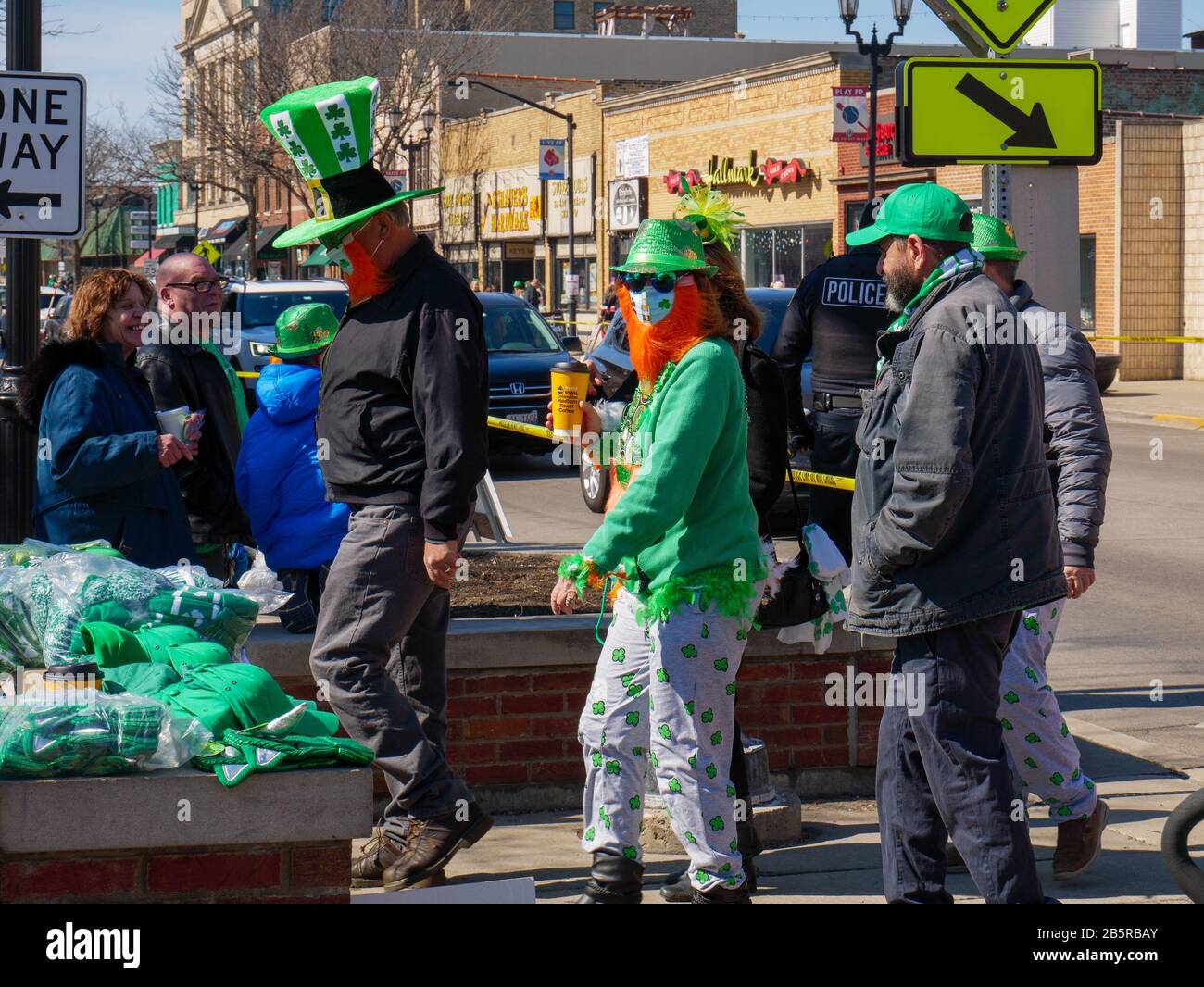 Forest Park, Illinois USA. März 2020. Die Leute in Saint Patrick's Day garb trugen auch medizinische Masken, eine mit einem Ausschnitt aus Corona-Bier auf Maske als Referenz zu Coronavirus bei der heutigen Saint Patrick's Day Parade. Stockfoto