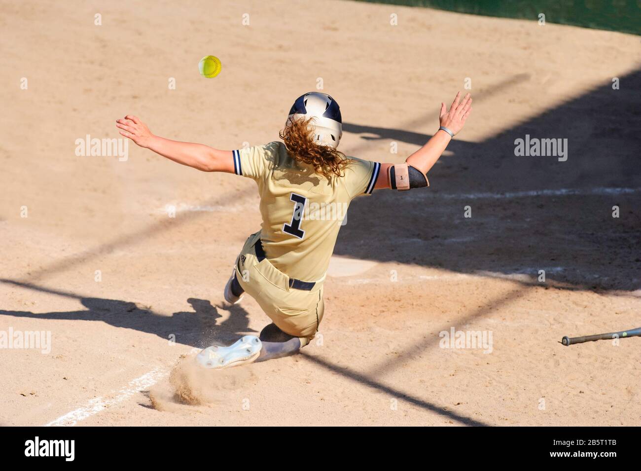 Ein Baseball-Spieler Schiebt Sich In die Home Base, Während der Ball Durch die Luft fliegt Stockfoto
