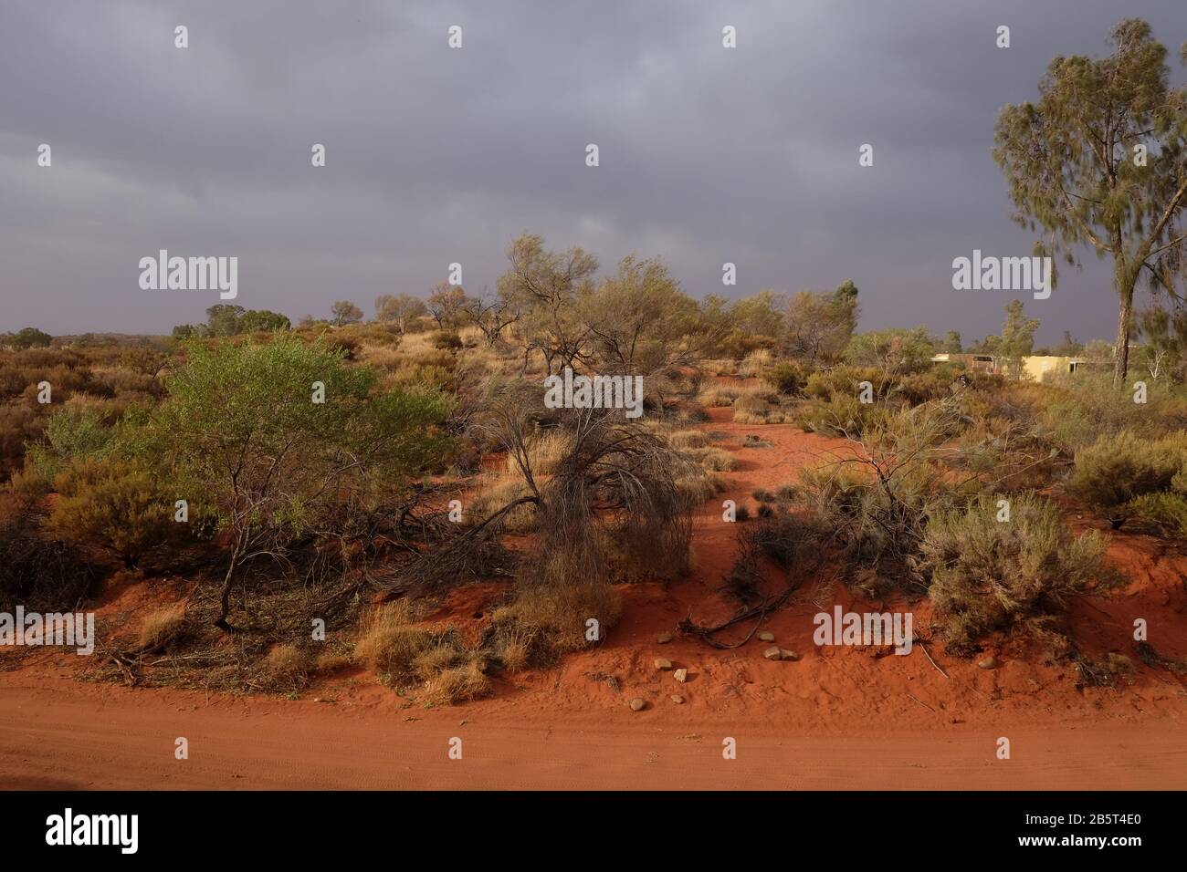 Dunkle Sturmwolken über einer roten Hügel- und Outback-Servicestraße, Gestrüpp- und Sandwege in Yulara, Sails in the Desert Resort, Northern Territory, Australien Stockfoto