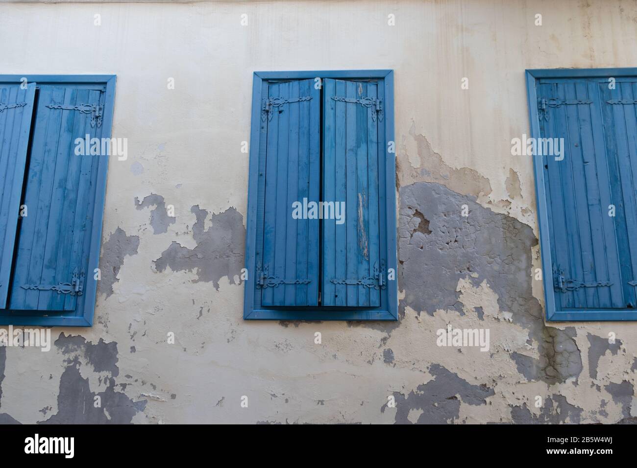 Drei blaue Fenster mit Blenden an einer schäbigen Wand Stockfoto