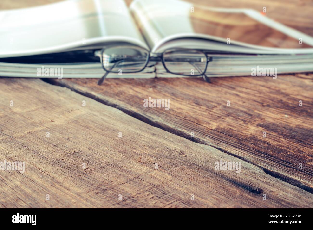 Ansicht der Zeitschrift oder des Katalogs, die mit einer Brille auf dem Holztisch gelesen werden kann. Konzept für Hintergrundtexturen Stockfoto