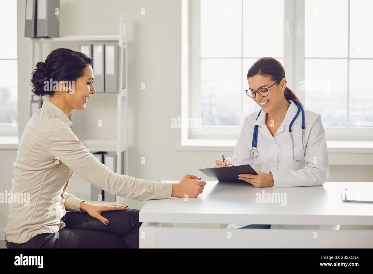 Ärztin Kinderärztin Gynäkologe spricht Klientin, die an einem Tisch in einer Klinik sitzt. Stockfoto