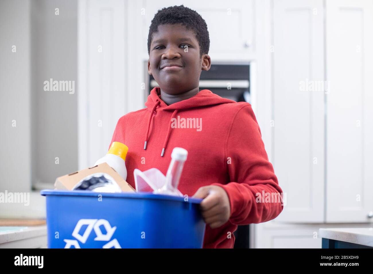 Portrait Des Jungen, Der In Der Küche Zu Hause Steht Und Den Recyclingbehälter Trägt Stockfoto