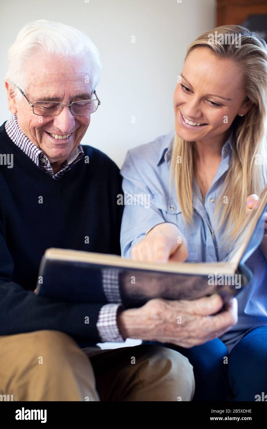 Großvater bei Fotoalbum mit Erwachsenen Enkelin Suchen Stockfoto