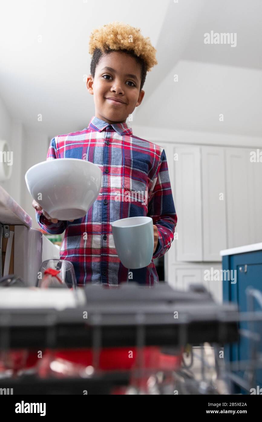 Portrait Of Boy Helfend With Chores At Home By Stacking Geschirr In Geschirrspüler Stockfoto