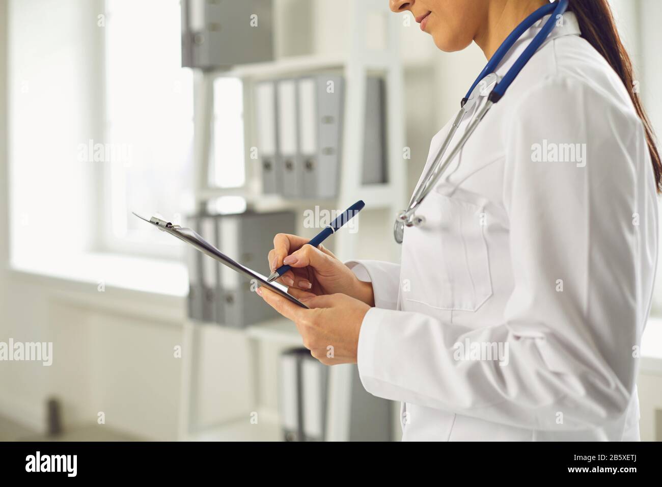 Gesichtslose Ärztin schreibt ein Rezept in die Zwischenablage, während sie im Klinikum steht. Stockfoto