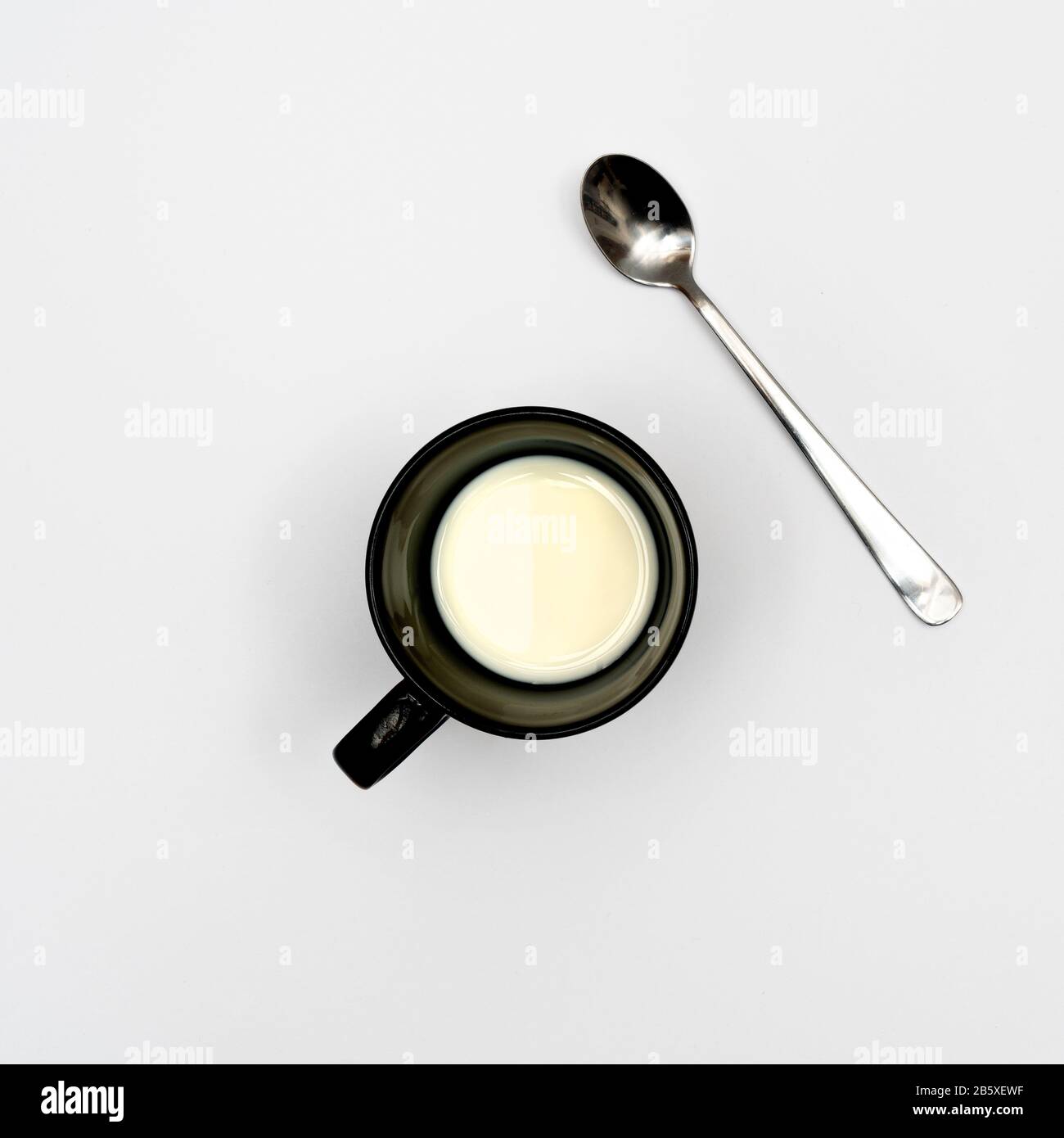 Eine Tasse Milch und ein Teelöffel auf einer weißen Oberfläche Stockfoto