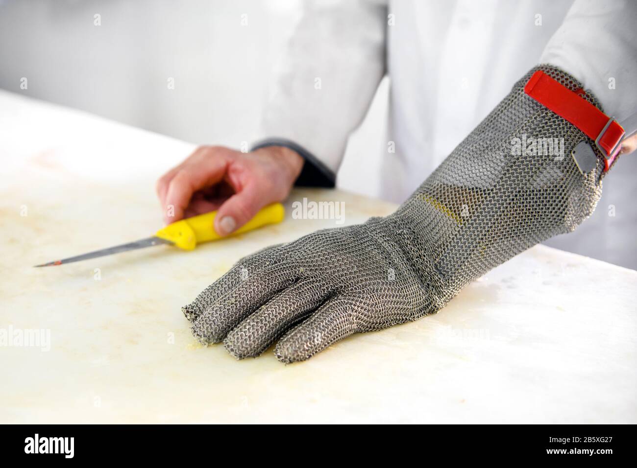 Schließen Sie einen Schutzhandschuh mit Metallgitter an einem Kettenpostenschneider, um Schnittwunden von Messern an der Hand eines männlichen Metzgers zu verhindern, der auf einem Schneidschwein ruht Stockfoto