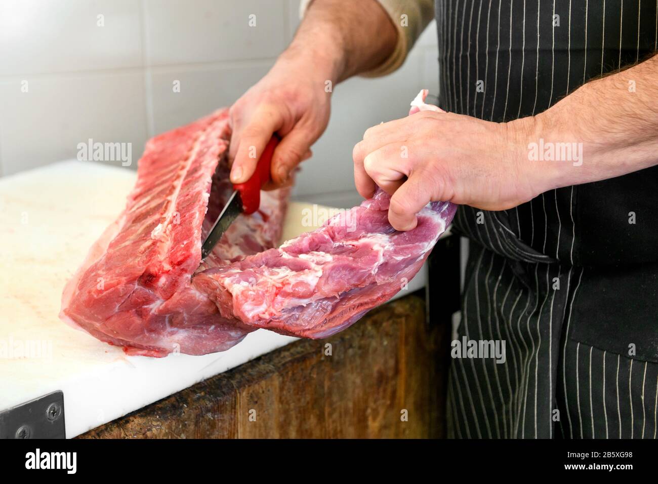 Metzger schlitzte ein rohes Schweinefilet mit einem scharfen Messer auf einem Metzgerblock in Nahaufnahme von seinen Händen vom Knochen Stockfoto