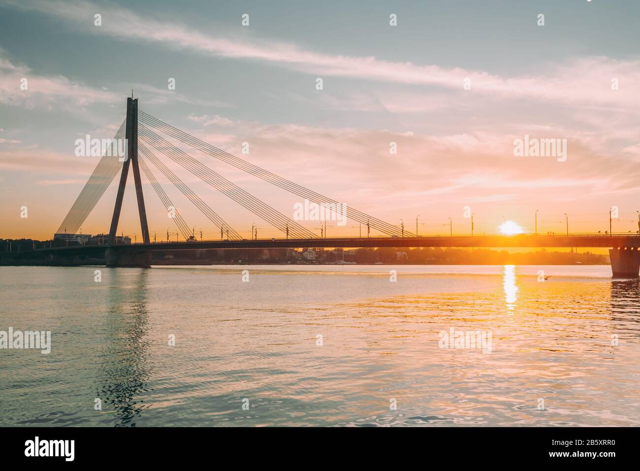 Riga, Lettland. Malerische Aussicht Vansu Kabel-gebliebene Brücke über den Fluss Daugava, westliche Dwina In leuchtenden Sonnenuntergang bis Sonnenaufgang Stockfoto