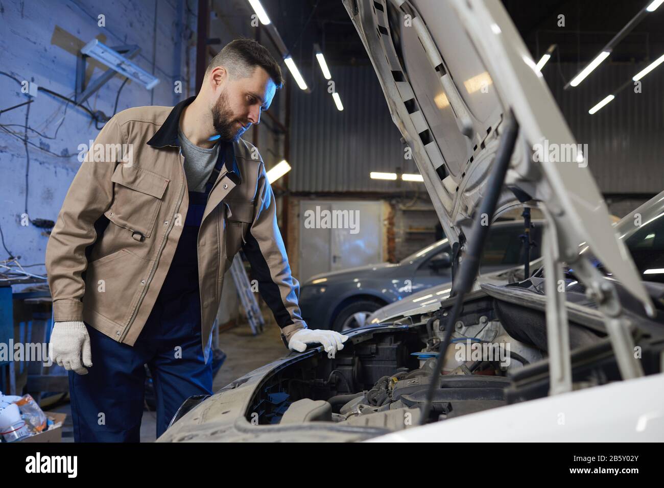 Horizontaler mittlerer langer Schuss professioneller Automechaniker mit gleichmäßigem Blick auf Automotor, Kopieraum Stockfoto