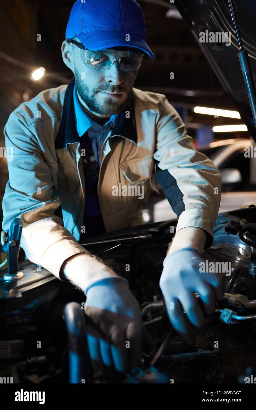 Vertikaler Schuss von reifen Autoservice-Spezialisten in Kaukasien mit Schutzuniform und Brille zur Befestigung moderner Motorteile Stockfoto