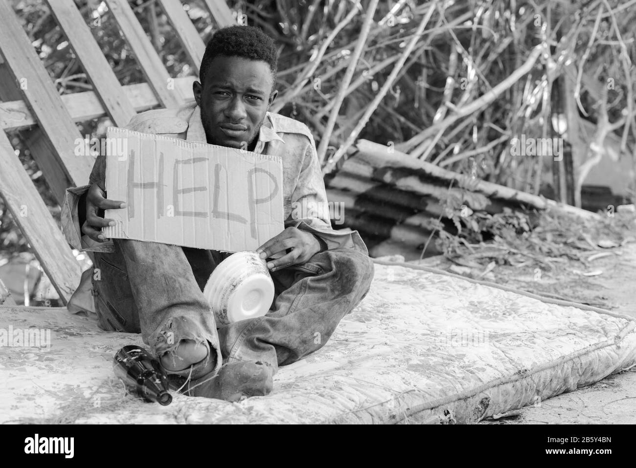 Junger obdachloser Afrikaner mit Pappschild, der in Schwarz-Weiß um Hilfe bittet Stockfoto