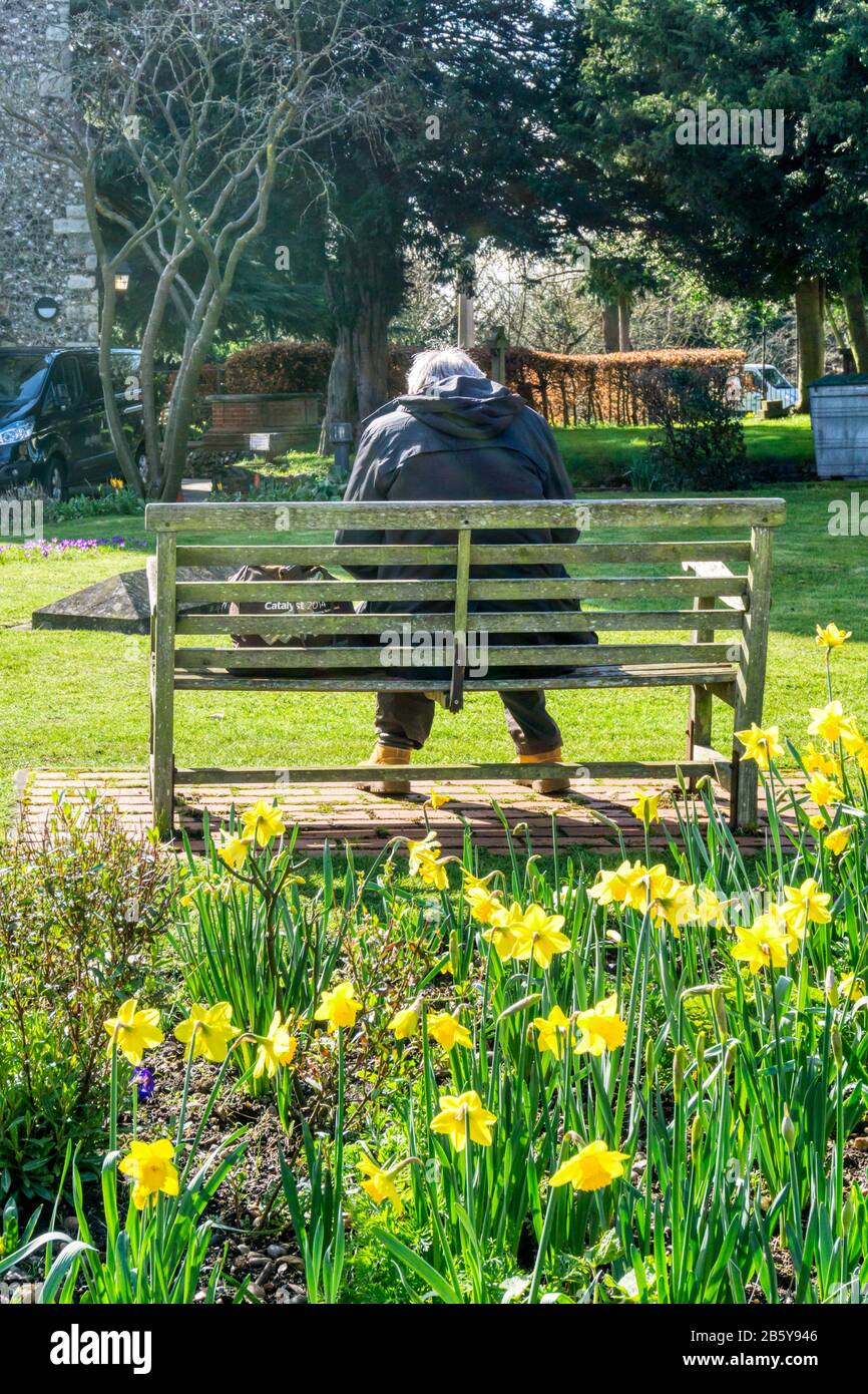 Senior man sitzt auf der Bank im Kirchhof, mit Frühlings-Narben. Stockfoto