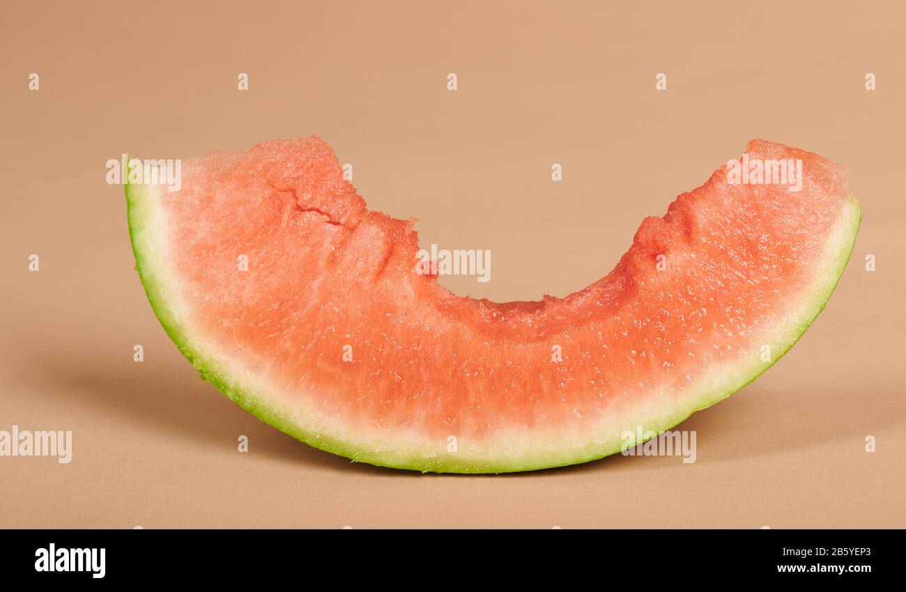 Ein Stück Wassermelone mit großem Biss auf beigefarbenem Studiohintergrund Stockfoto
