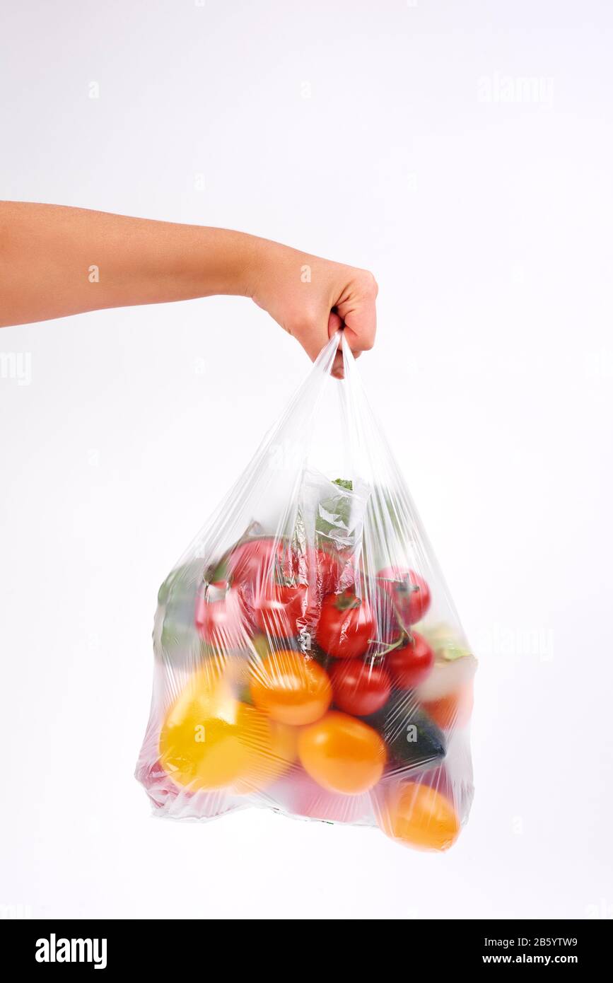 Die Hand der Frau, die Plastiktüten mit Gemüse auf weißem Hintergrund hält Stockfoto
