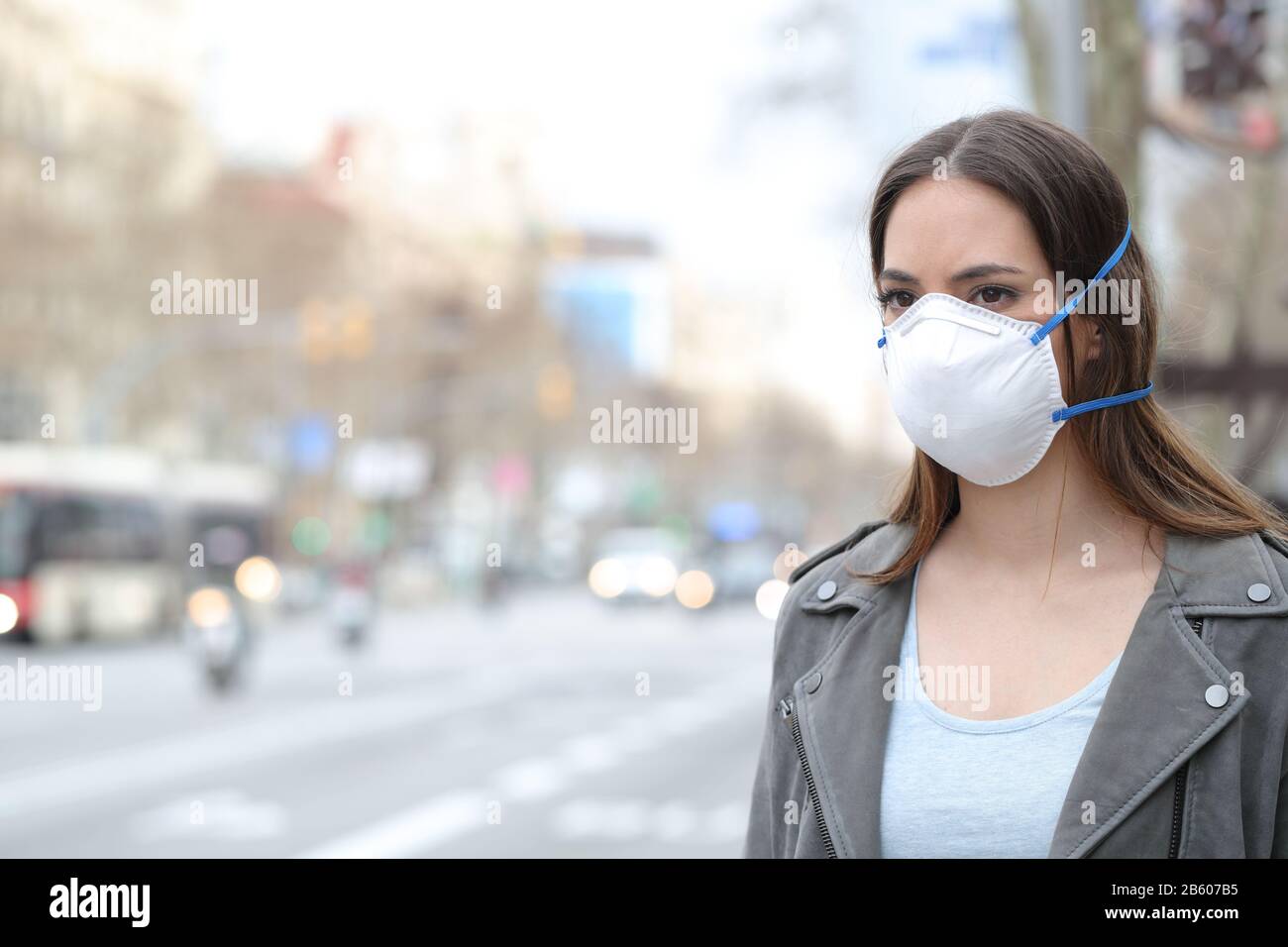 Ernste Frau, die Schutzmaske trägt, um Verschmutzungen zu vermeiden, die auf die Straße in der Stadt blicken Stockfoto