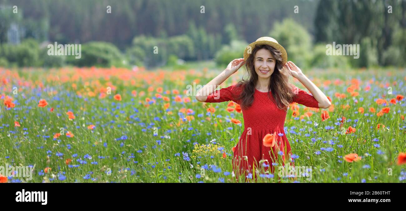Verträumte Frau in rotem Kleid und Hut in wunderschönem Mohnfeld mit Kräuterblüte. Klassisch-eleganter Romantiklook, das Konzept des schönen Sommers. Panorama-Banner Stockfoto