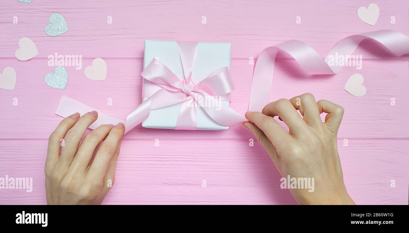 Valentinstag Liebe Konzept der Schönen womans Hände halten Geschenkbox Handwerk Papier und Herz Konfetti auf rosa Hintergrund. nach oben Blick flach mit Platz für Stockfoto