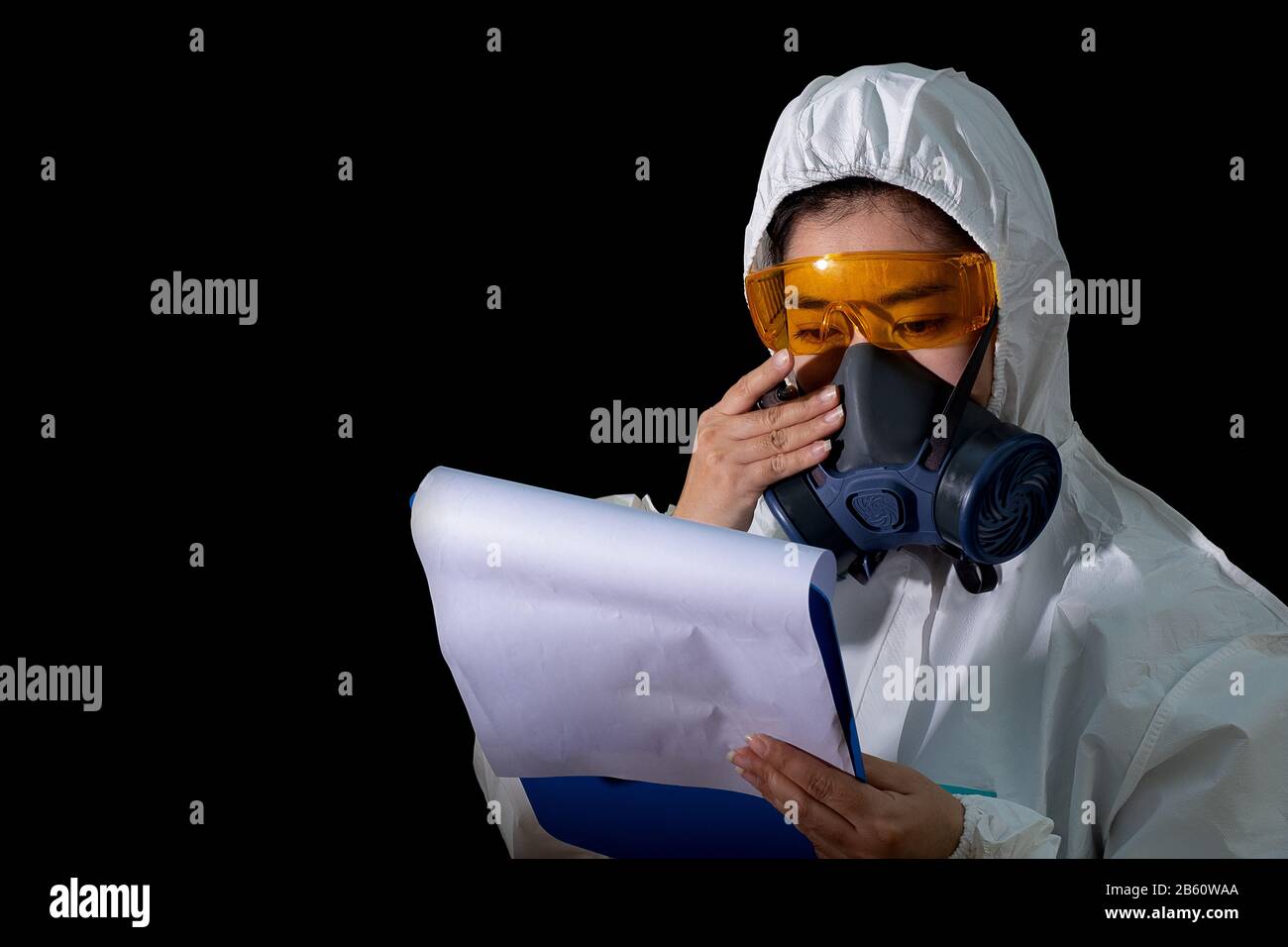 Frau hält Berichtsordner in weißer chemischer Schutzkleidung und Gasmaske mit gelber Brille auf schwarzem Hintergrund, Wissenschaftlerin in Safet Stockfoto
