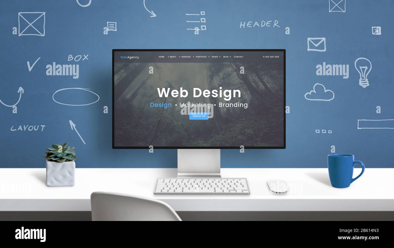 Webdesign Studio Homepage auf modernem Computermonitor. Büroschreibtisch mit Zeichnungen von Webdesignelementen an der Wand Stockfoto