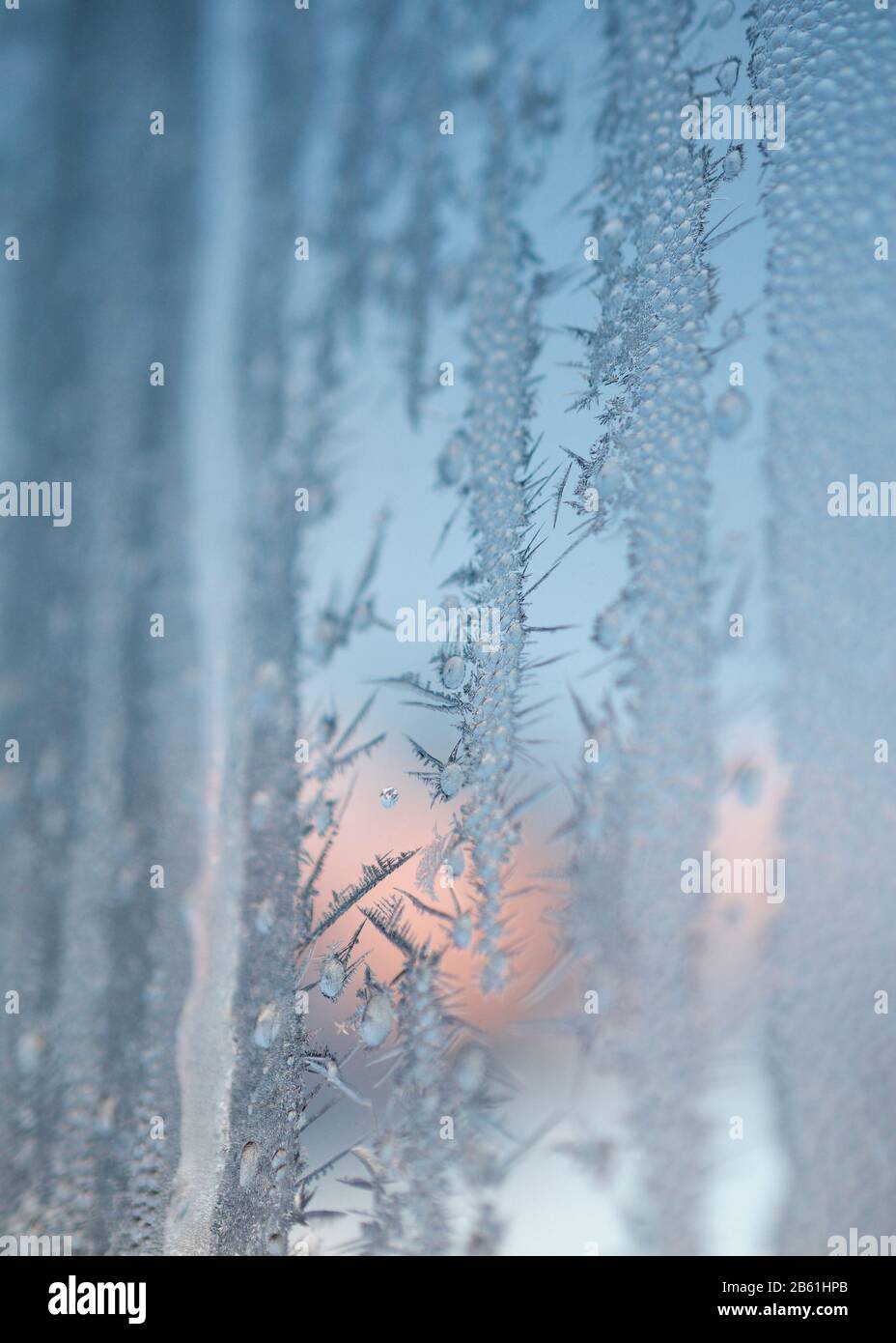 Verhalbauter Winteraufgang durch Fenster, das von Eisblumen bedeckt ist. Wählen Sie Fokus. Stockfoto