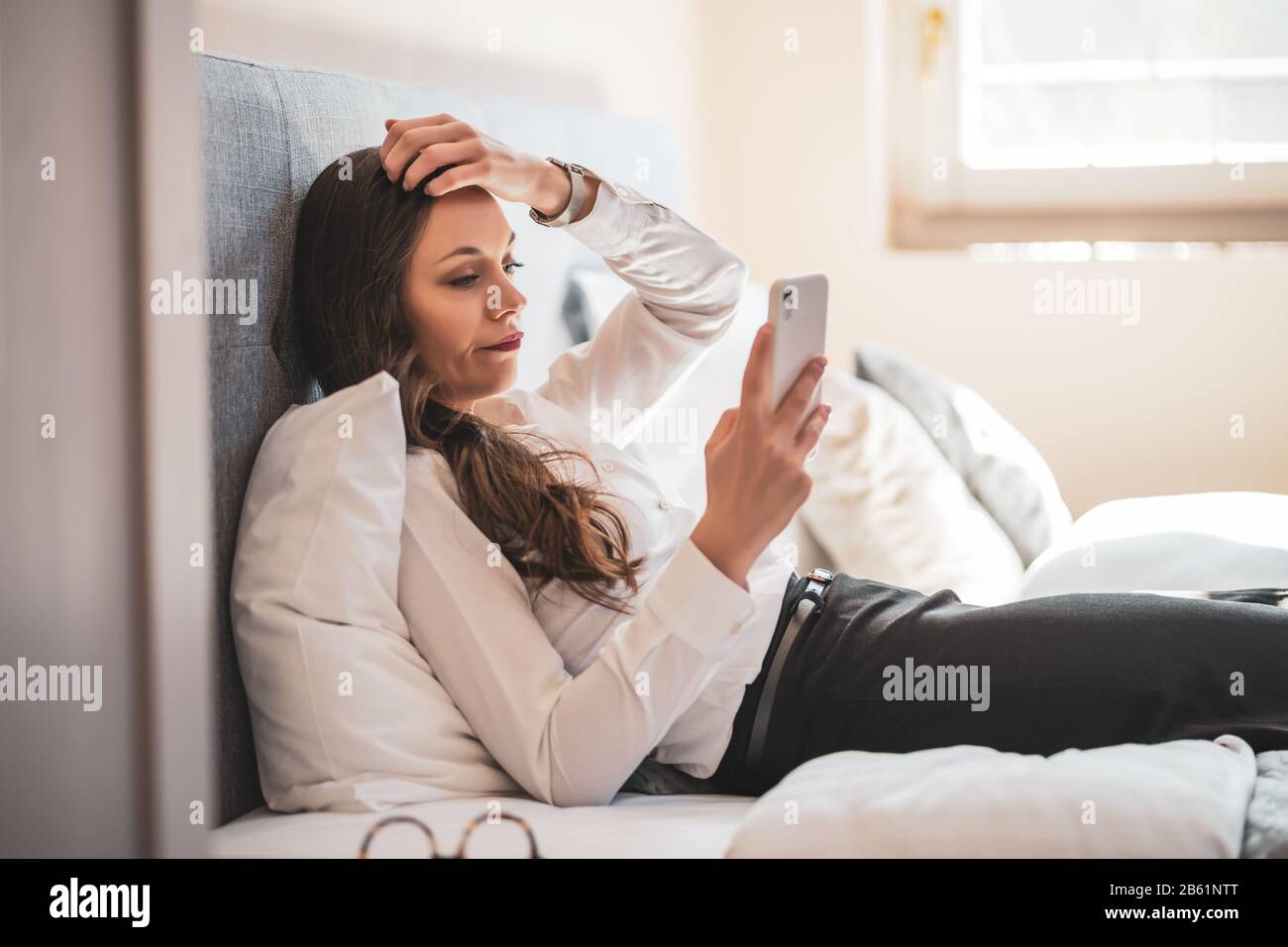 Besorgte Geschäftsfrau auf Geschäftsreise im Hotelzimmer und mit Smartphone. Stockfoto