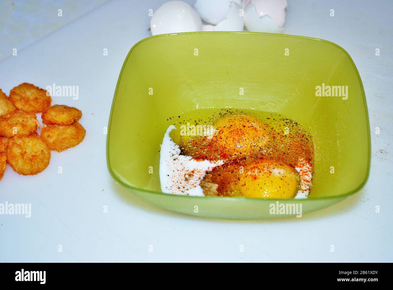 Nahaufnahme von zwei rohen, gewürzten Eiern in einer grünen Plastikschale mit Röstis und Aubergschalen Stockfoto