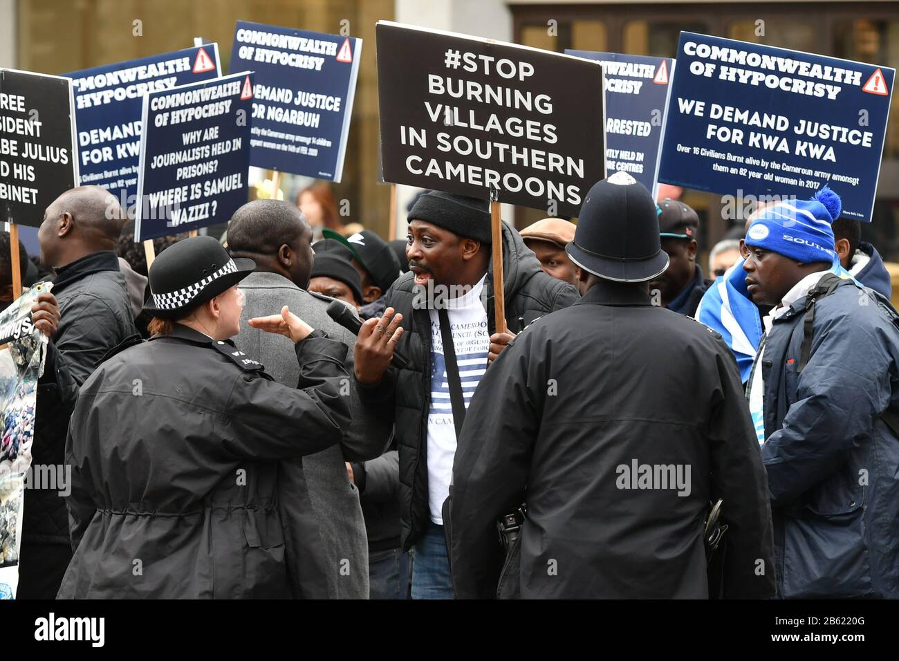 Polizisten sprechen mit Demonstranten, die vor dem Commonwealth Service Plakate mit Nachrichten über Kamerun außerhalb der Westminster Abbey, London, halten. Stockfoto