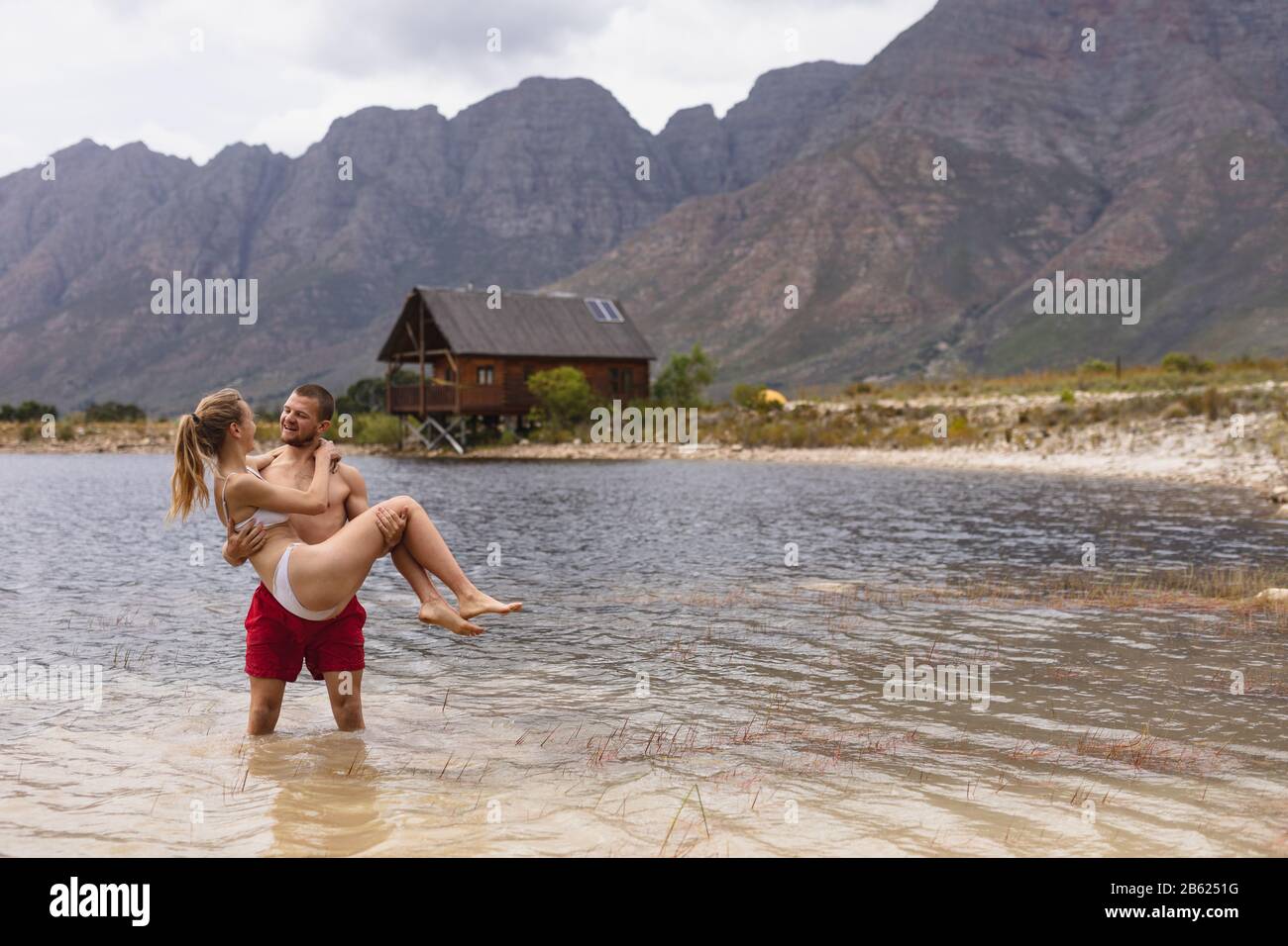 Kaukasischer Mann hält seine Frau am See in der Nähe des Holzschuppens Stockfoto