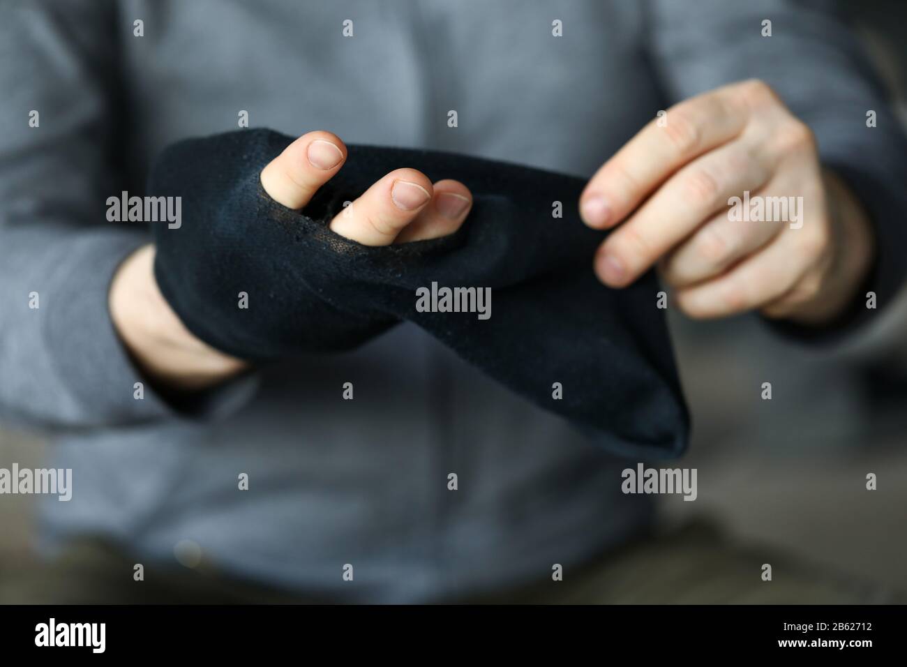 Man passiert die Finger durch das große Loch in der schwarzen Socke Stockfoto