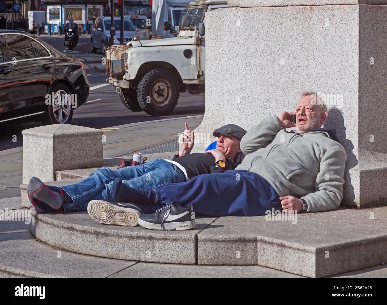 London, Westminster. Zwei Männer, die sich bei Sonnenschein auf dem Sockel der Edith-Cavell-Gedenkstätte am St. Martin's Place entspannen. Stockfoto