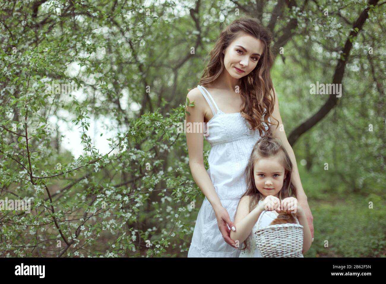Junge schöne Mutter und ihre Tochter stehen im Wald. Das Kind hält einen Korb mit einem Kaninchen. Stockfoto