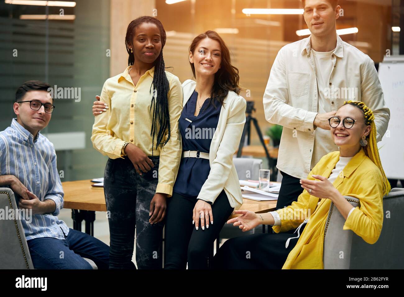 Gruppe glücklicher erfolgreicher Erwachsener, die ungezwungene Kleidung tragen und im Büro stehen und sich gegenseitig umarmen, sich vor die Kamera posieren. Lieblingskollegen Stockfoto