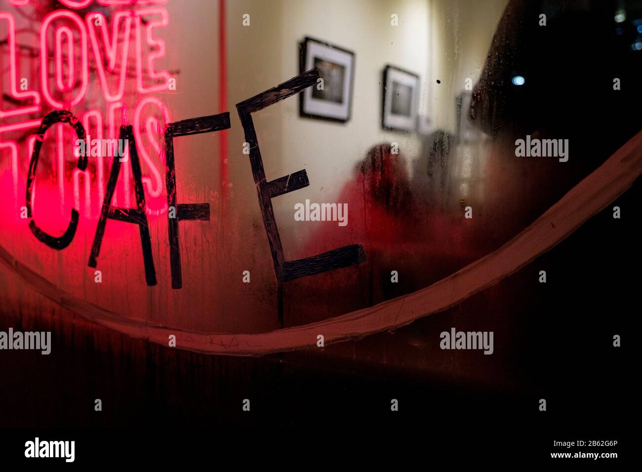 Ein Straßenfenster eines Cafés in der Nacht mit einem rosa Neonlicht, das "LOVE THIS CAFE" sagt. Stockfoto