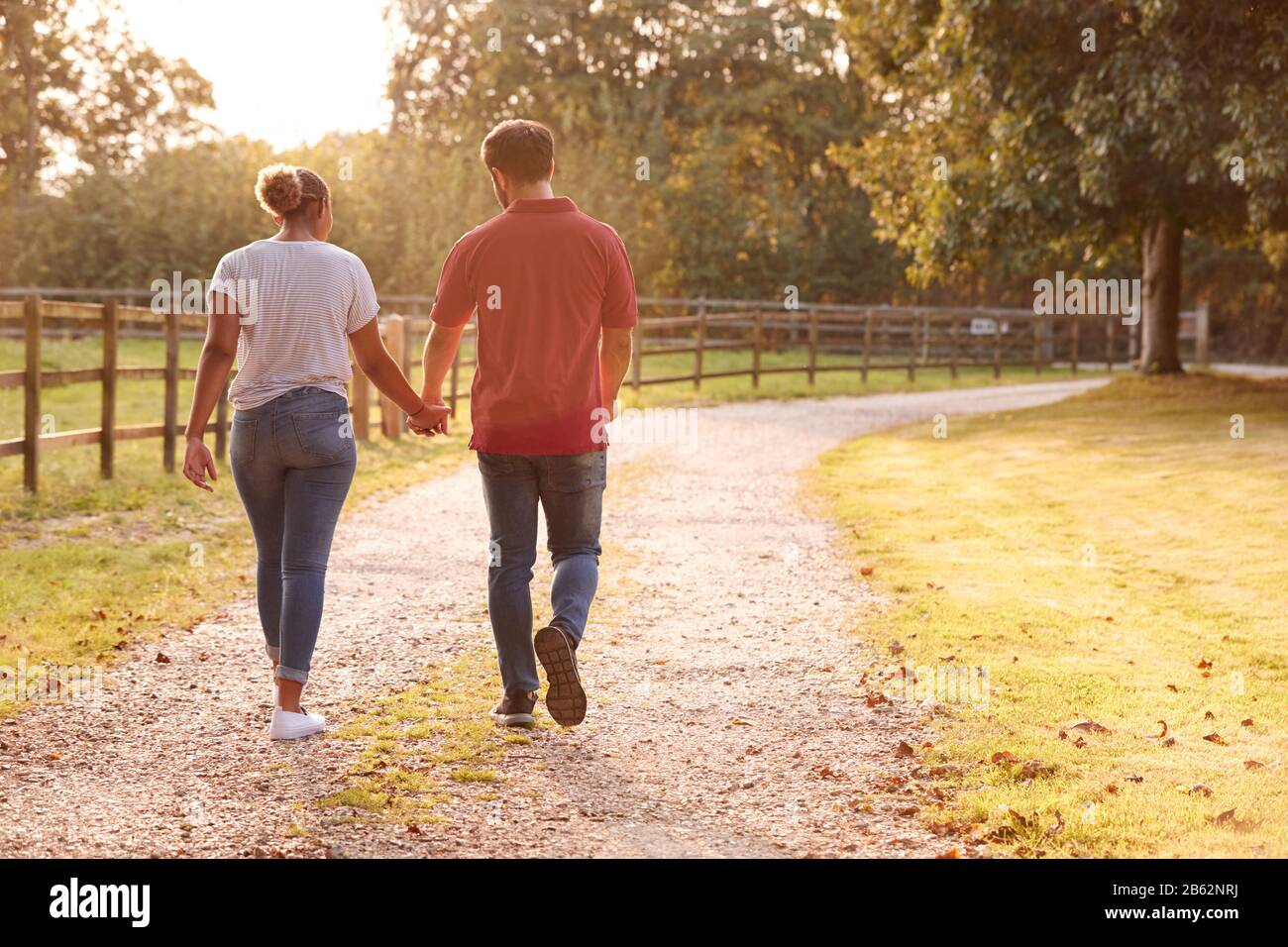 Rückansicht Eines Romantischen Ehepaares Bei Sonnenuntergang Hand In Hand Entlang Der Country Lane Stockfoto