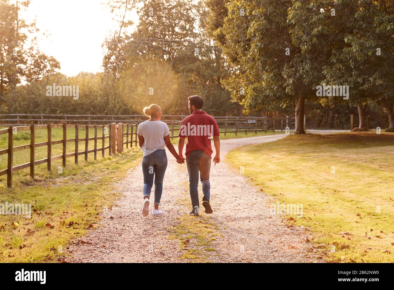 Rückansicht Eines Romantischen Ehepaares Bei Sonnenuntergang Hand In Hand Entlang Der Country Lane Stockfoto