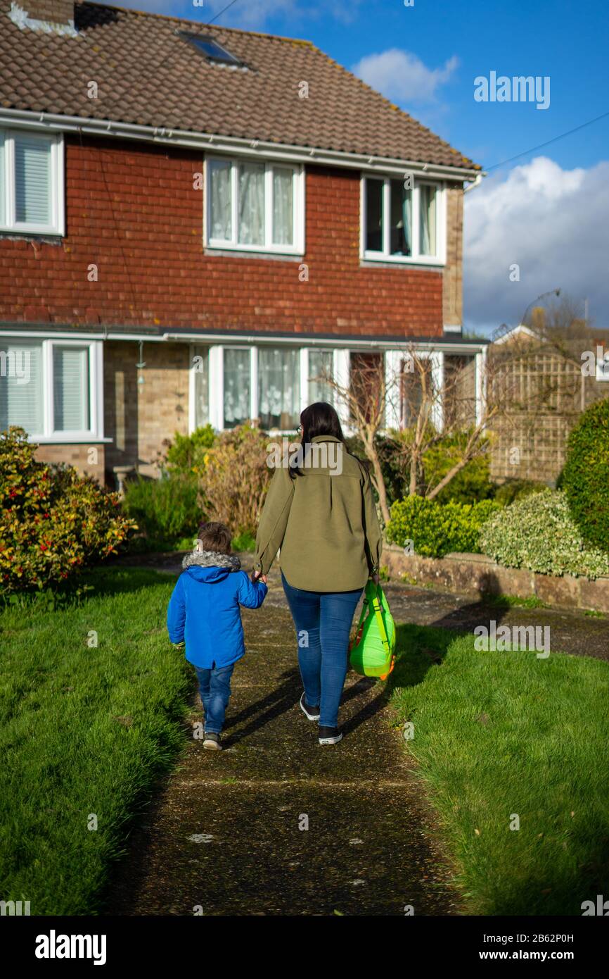 Eine Mutter und ein junger Sohn halten die Hände, die einen Gartenpfad zu einem Haus hinauf gehen Stockfoto