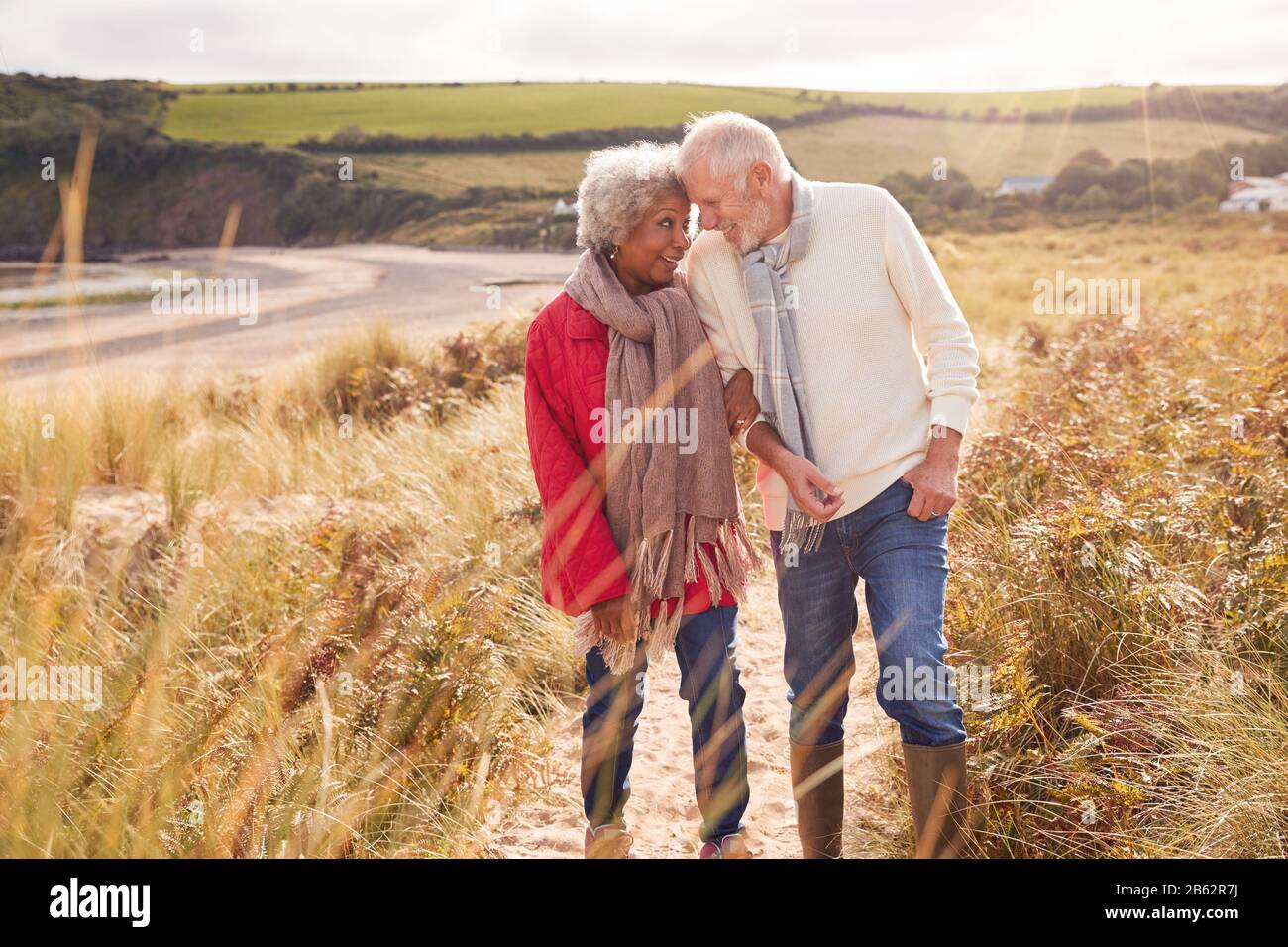 Liebevolles Aktives Älteres Paar, Das Arm In Arm Durch Sanddünen Im Winter Beach Urlaub Geht Stockfoto