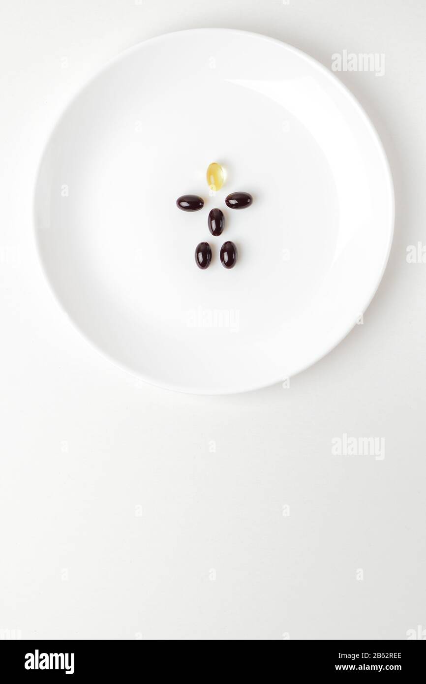 Astaxanthin- und Fischölpillen bilden auf der weißen Platte eine menschliche Form. Nahaufnahme. Kopierbereich unten. Stockfoto