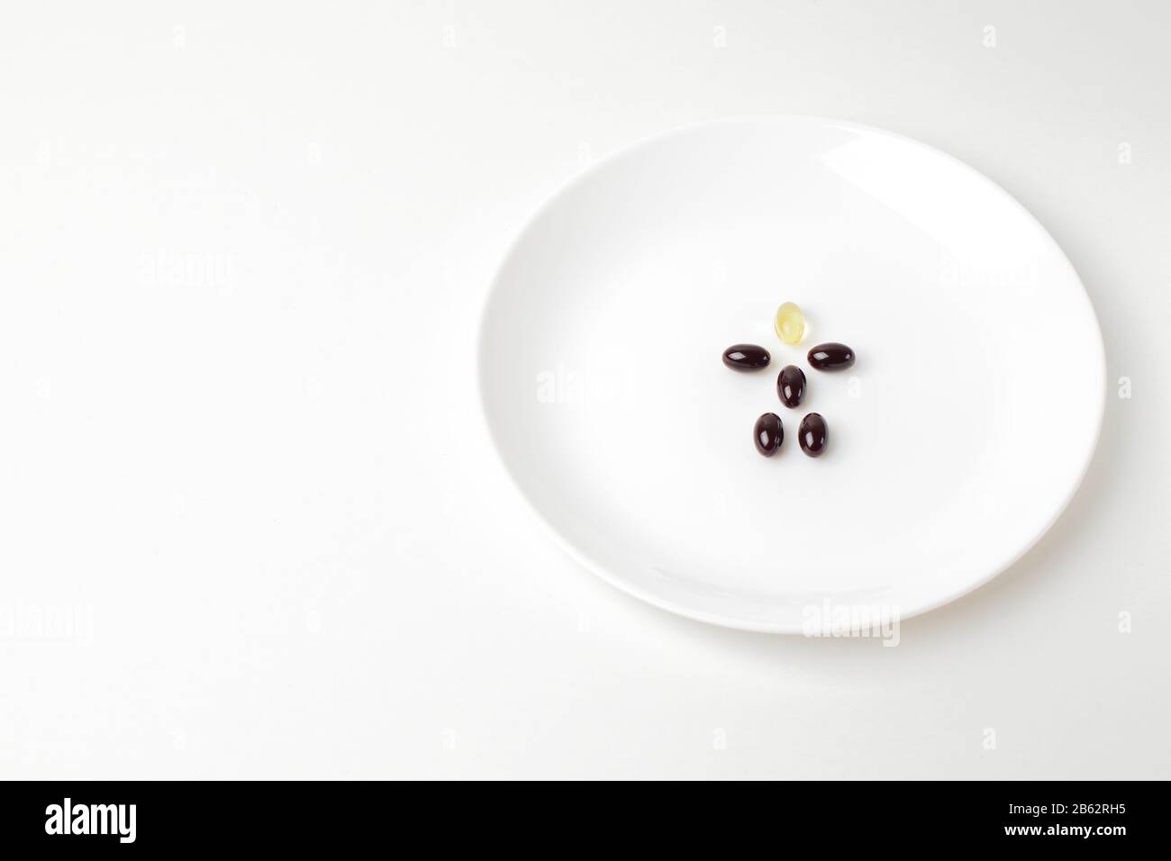 Astaxanthin- und Fischölkapseln bilden auf der weißen Platte eine menschliche Form. Nahaufnahme. Stockfoto