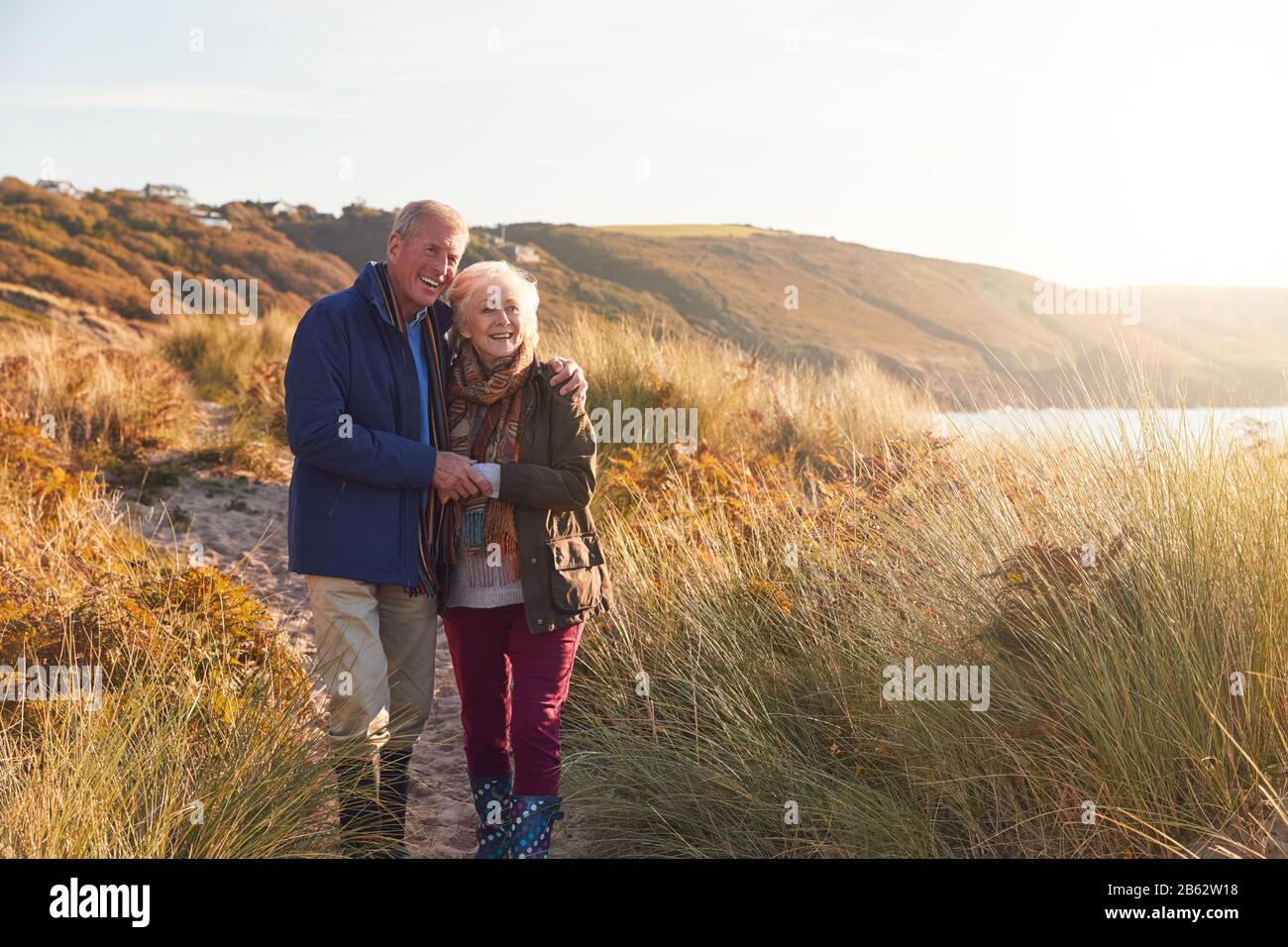 Liebevolles Aktives Älteres Paar, Das Umarmt, Während Sie Durch Sanddünen Gehen Stockfoto