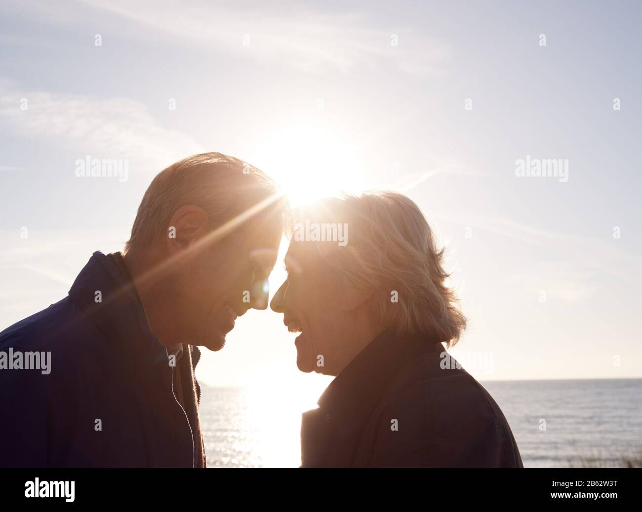 Liebevolles Aktives Älteres Paar, Das Hände Hält, Während Sie Durch Sanddünen Gegen Die Aufflackernde Sonne Gehen Stockfoto