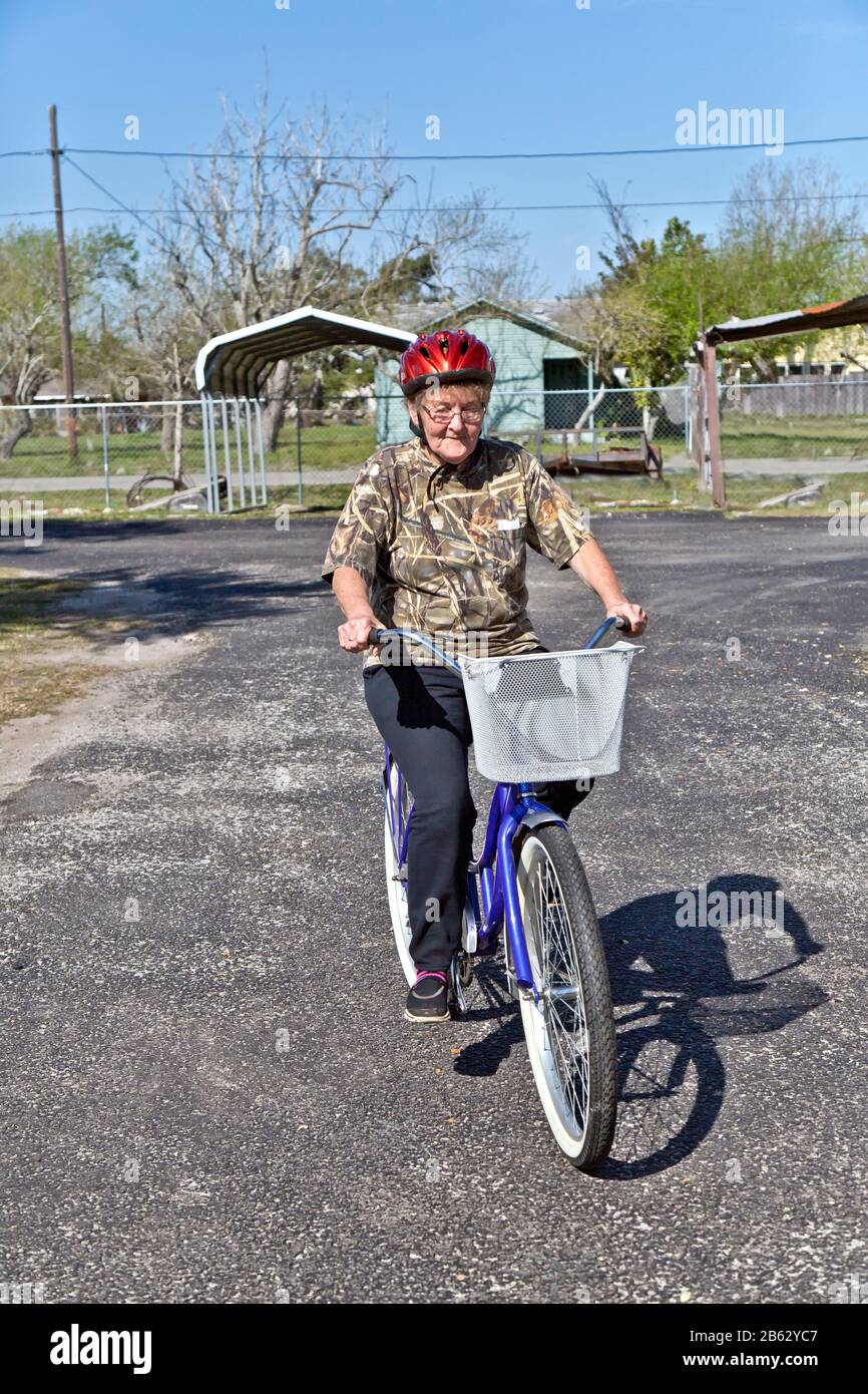 Ältere Frau, die Schutzhelm trägt, lernt, ihr neu erworbenes gespendetes Fahrrad zu fahren. Stockfoto